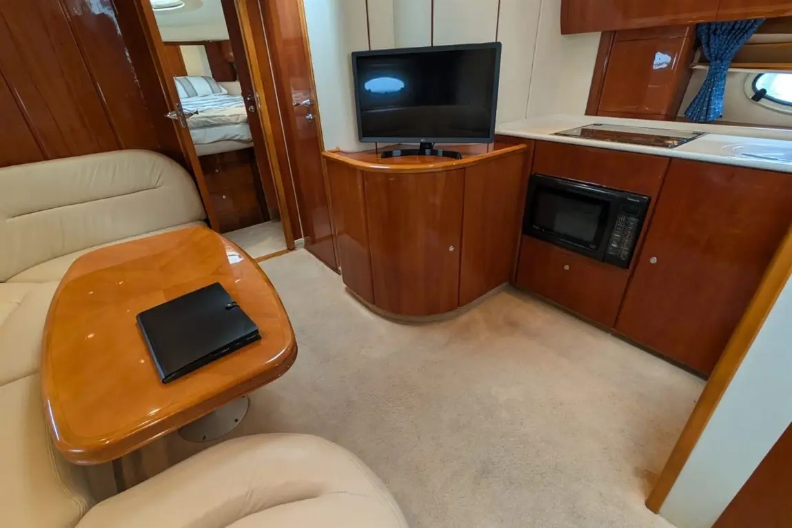 Interior of a yacht, featuring a leather sofa, wooden table, TV, and kitchenette with microwave, in a light and spacious design.