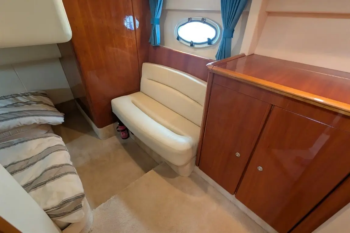 Interior of a boat cabin featuring a double bed with striped bedding, a leather bench, and wooden furniture with storage.