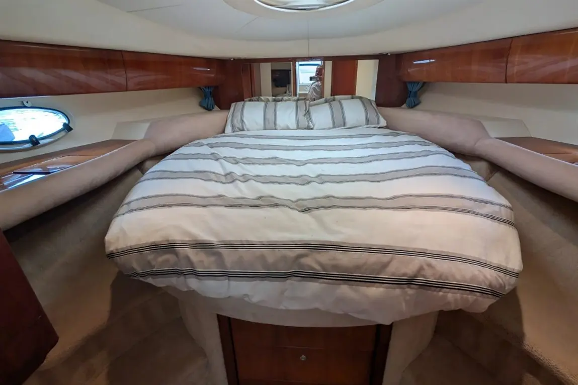 Interior cabin of a boat featuring a large, striped double bed, polished wood finishes, and soft lighting.
