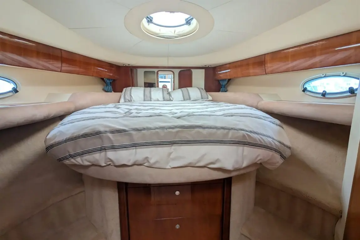 Cosy boat cabin featuring a large round bed with striped bedding, wooden cabinetry, and porthole windows.