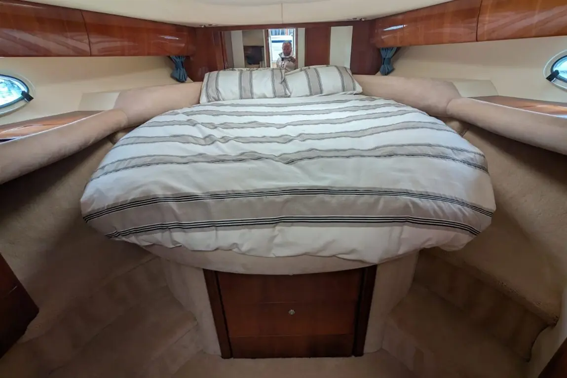 A cosy boat cabin featuring a circular bed with striped bedding, wooden cabinetry, and two circular windows.