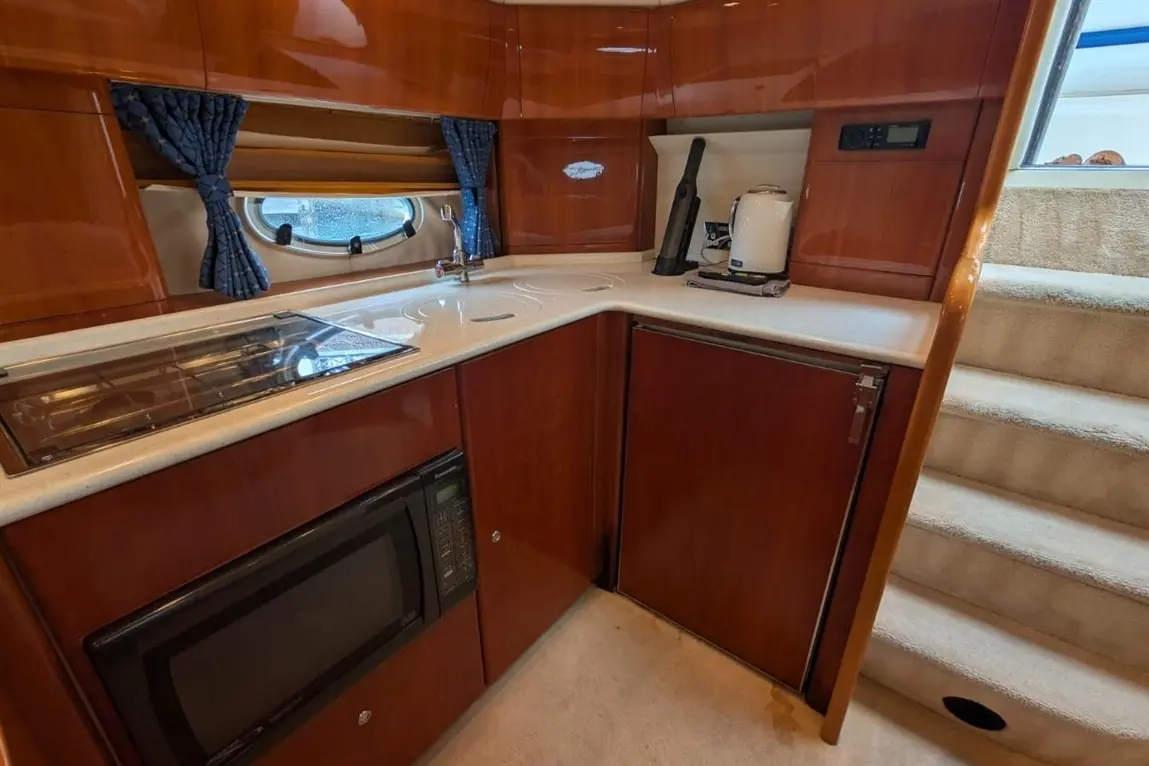 Modern boat kitchen featuring a fitted sink, microwave, stove, kettle, and curtains, with stairs leading out of the area.