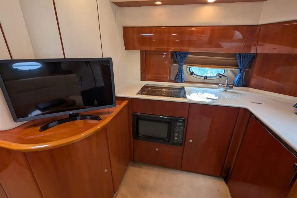 Modern boat kitchen featuring a TV, microwave, stove, and an oval window with curtains, all set in rich wooden cabinetry.