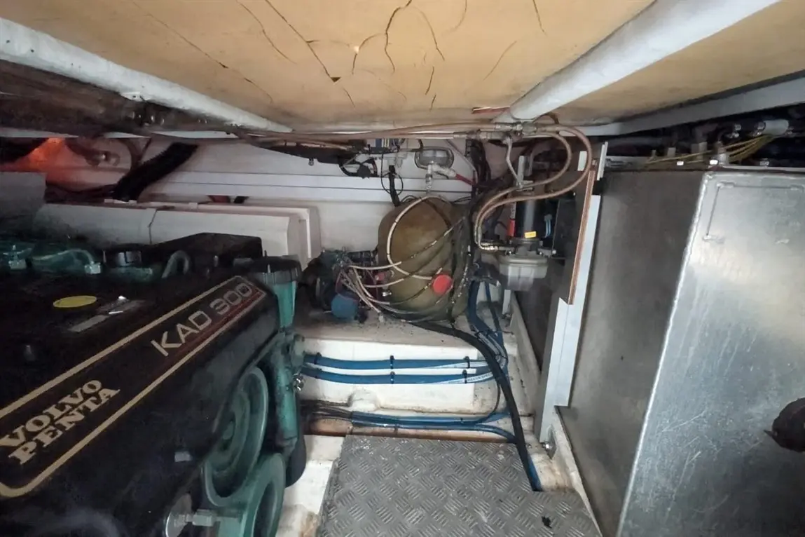 Boat engine compartment featuring a Volvo Penta KAD 300 engine, pipes, and a circular tank with wires and tools visible.