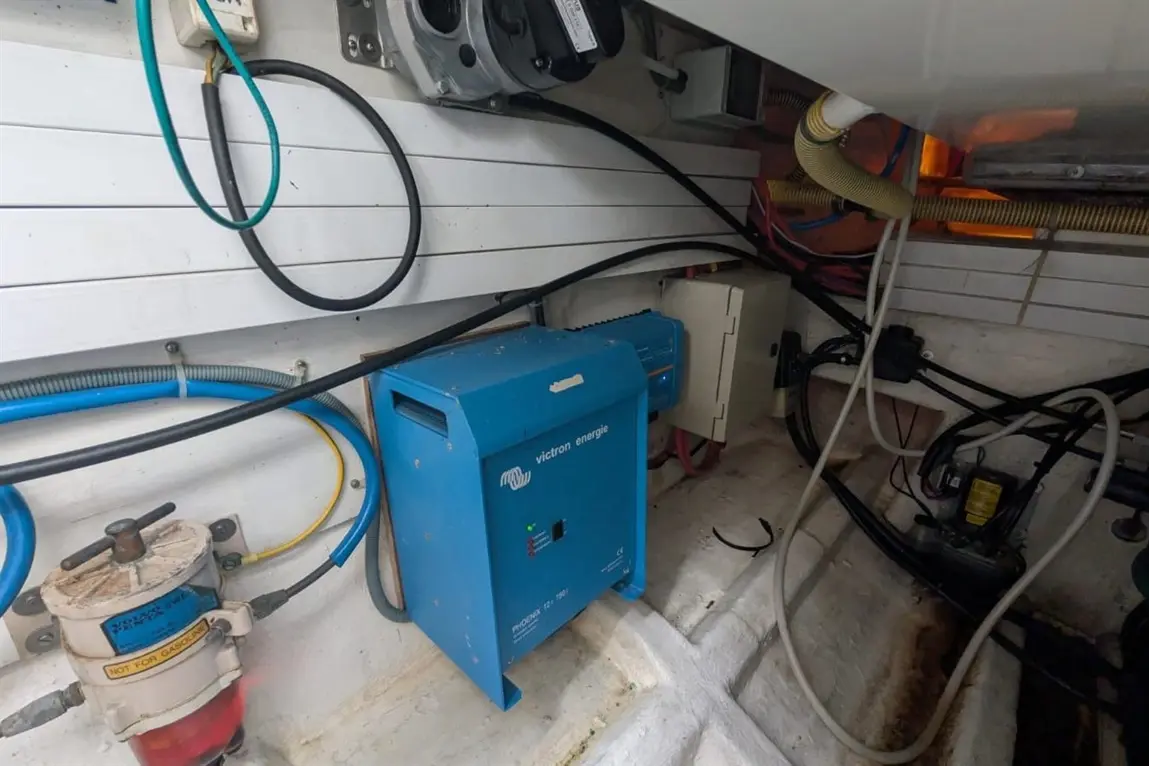 Inside a boat, showing a Victron Energy inverter, interconnected cables, and plumbing components on the wall.