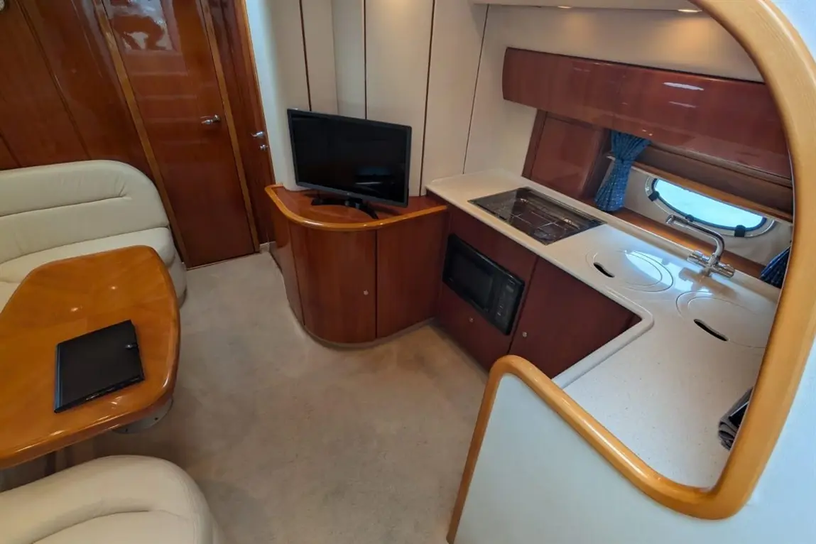 Interior view of a modern boat cabin featuring a kitchenette, a television, a dining area, and wooden furnishings.