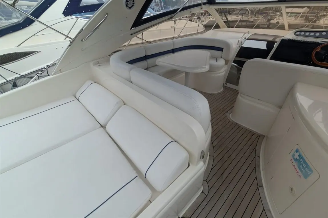 Luxurious yacht interior featuring white seating, a circular table, and wooden decking, with boats visible in the background.