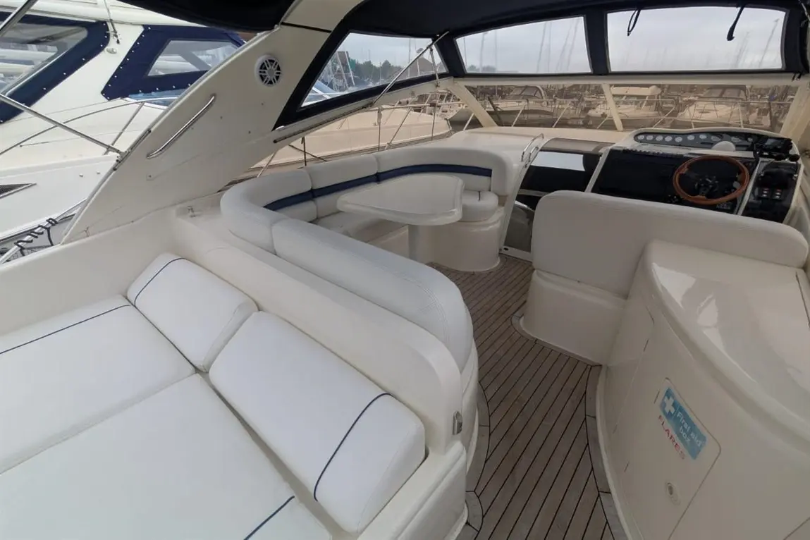 Luxury boat interior showing white seating, a small table, and a helm with navigational controls and a wood steering wheel.