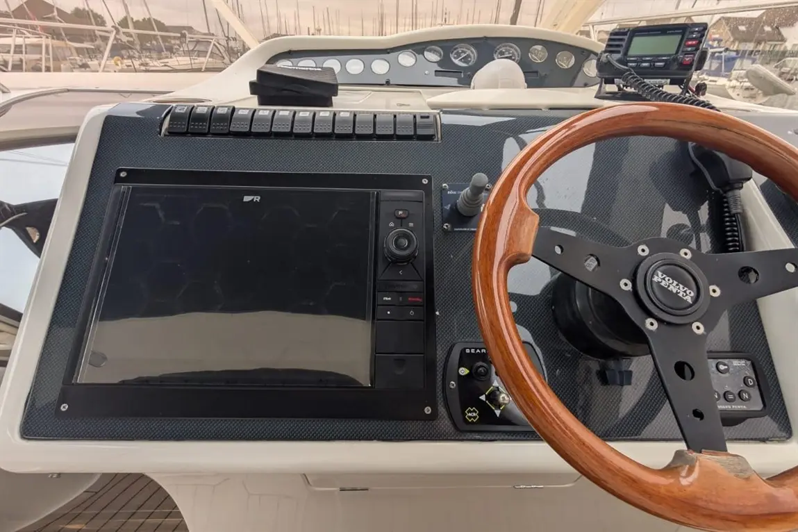 Boat dashboard featuring a wooden steering wheel, control panel, and a large display with navigation controls.