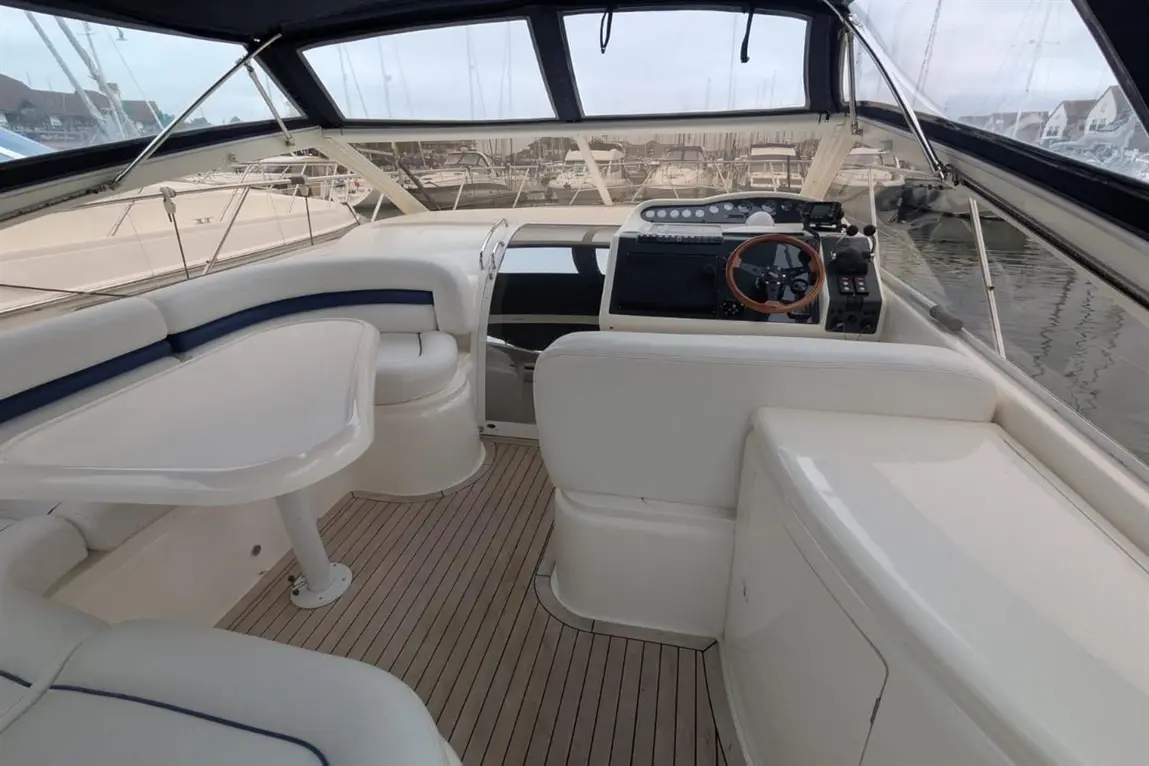 Interior of a luxurious boat featuring a white and navy seating area, navigation console, and marina view through large windows.