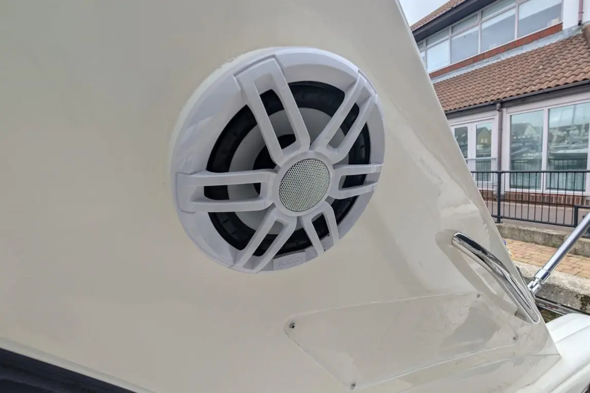 A close-up of a white marine speaker mounted on a boat, showing a sleek design against a light background.