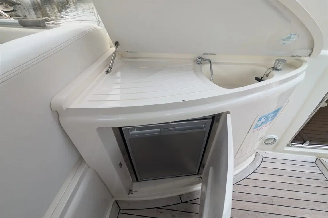 A boat kitchenette featuring a sink, storage compartment, and an integrated fridge on wooden deck flooring.