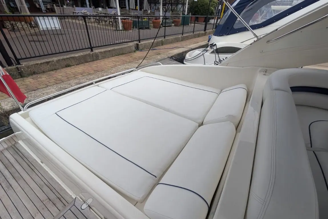 Luxury boat seating with white cushions and navy piping, overlooking a waterfront area with dining chairs and a flag.
