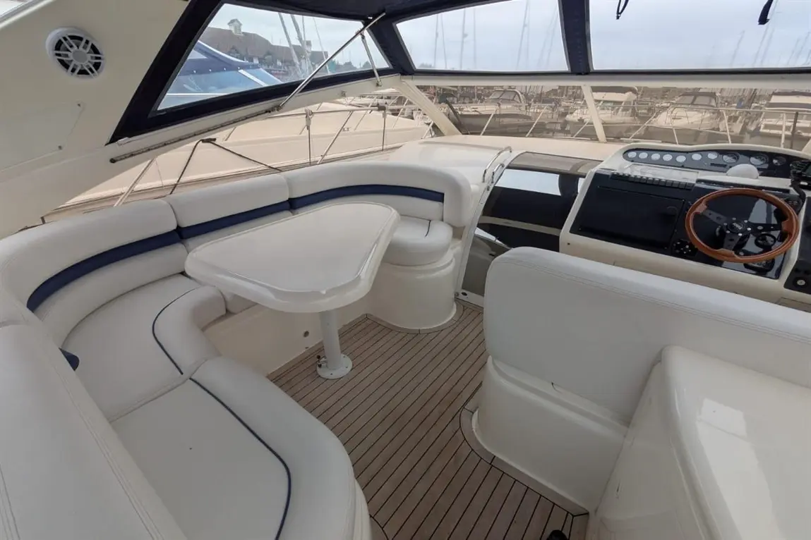 Luxury boat interior featuring a stylish lounge seating area, a table, and a well-equipped helm with a wooden steering wheel.