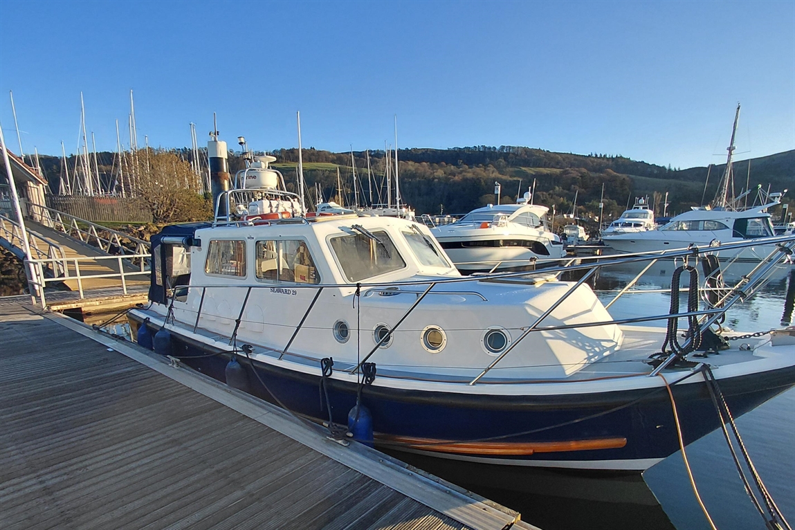A white Seaward 29 boat docked beside a wooden pier, surrounded by other boats in a marina under a clear blue sky.