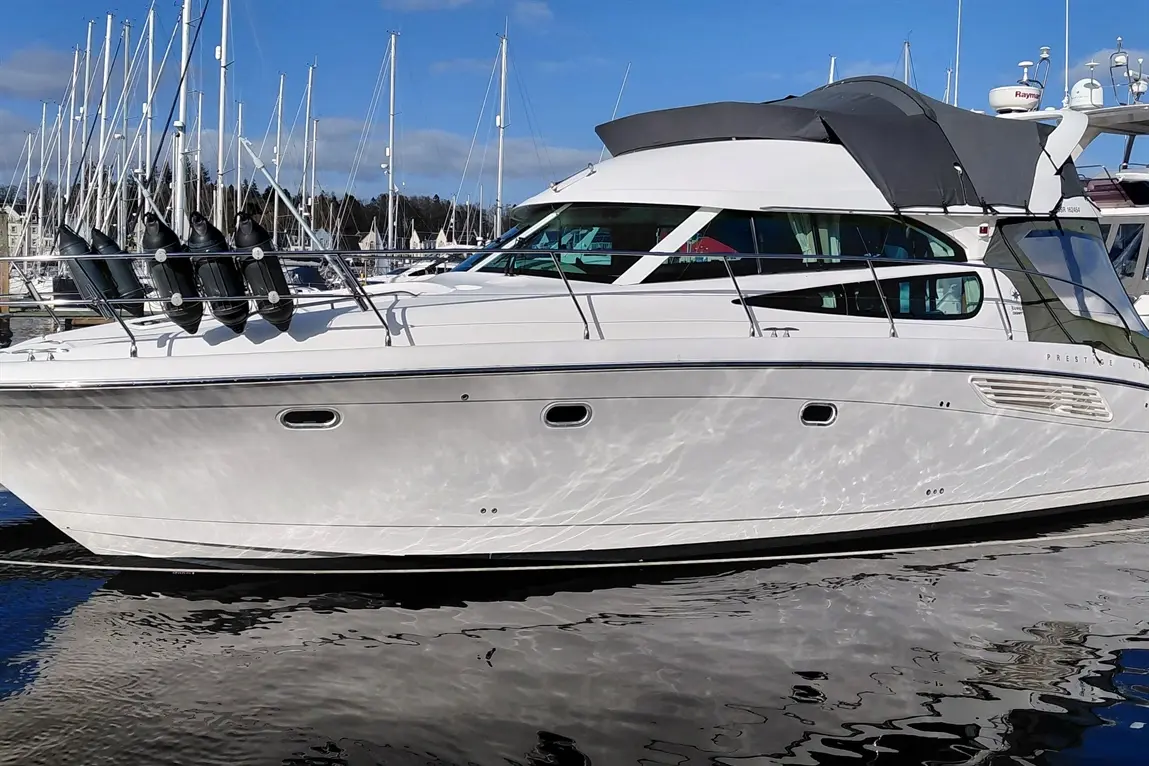 Motor yacht docked, featuring a sleek white exterior, black fenders, and a grey canopy under a clear blue sky.