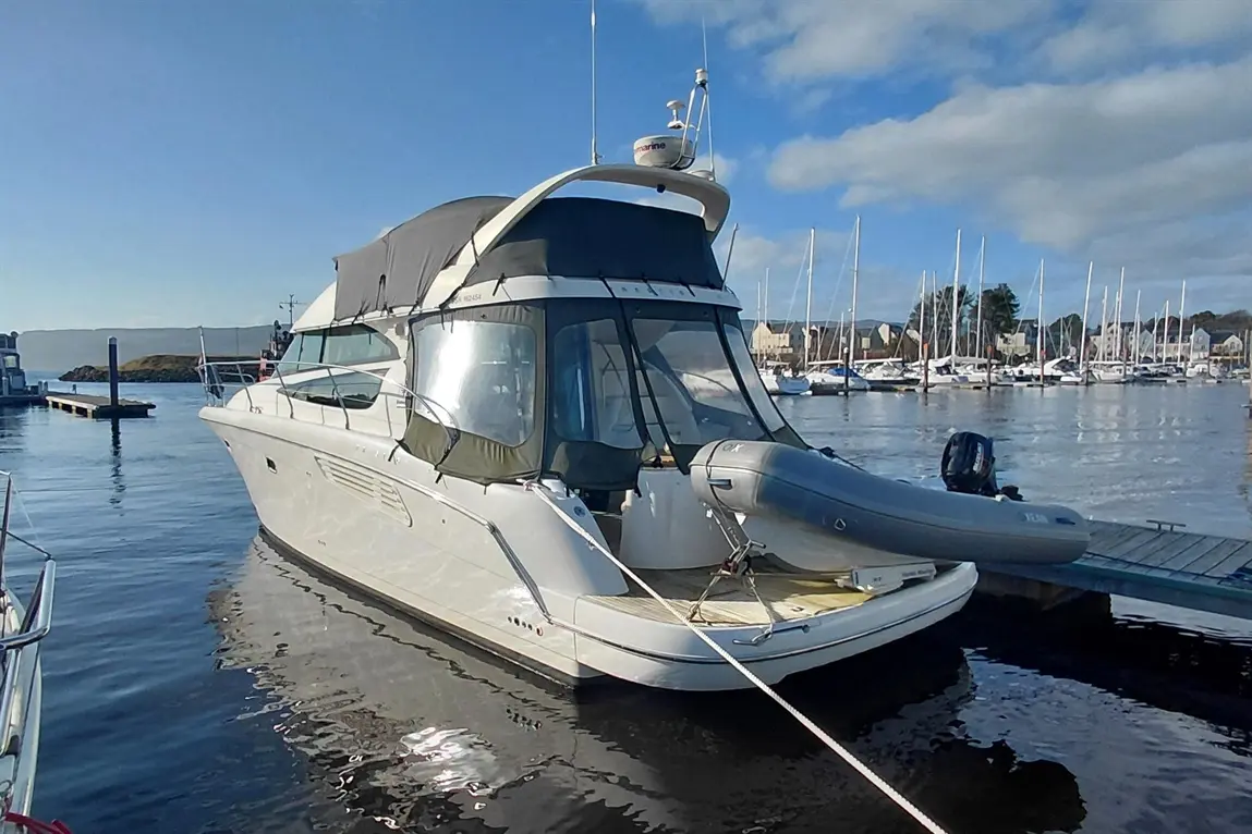 White motorboat docked in a marina, reflecting clear blue sky and other boats in the background.