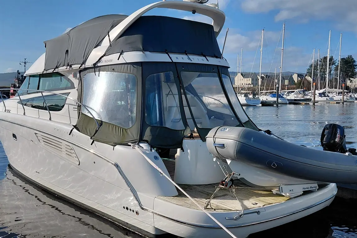 A sleek white motorboat docked at a marina, featuring a grey canopy and an inflatable dinghy attached at the rear.