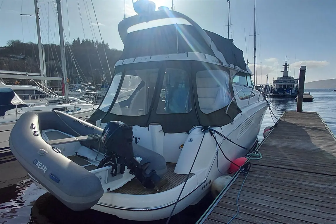 A white motorboat docked at a marina, featuring a grey inflatable dinghy with the text "OCEAN" and a scenic waterfront backdrop.