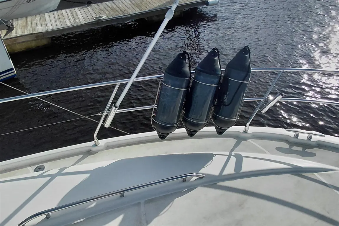 Three black fenders are secured on a boat railing, with a wooden dock and water visible in the background.