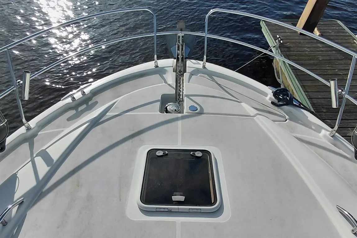 View from the bow of a boat, showcasing the deck, anchor, and reflective water surface. A hatch is visible on the deck.