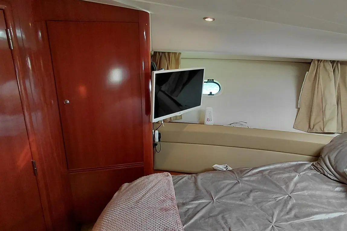 Interior of a boat cabin featuring wooden panels, a wall-mounted TV, a window, and a neatly made bed with a textured cover.