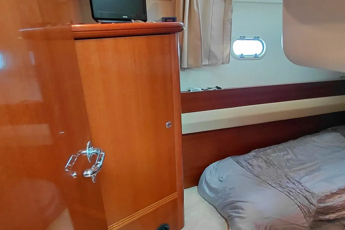 Interior of a boat cabin featuring a wooden wardrobe, a grey bedspread, and a small window with light coming through.