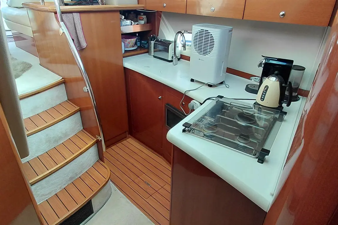 Interior view of a boat's kitchen, featuring a stove, coffee maker, toaster, and a staircase leading to the upper deck.