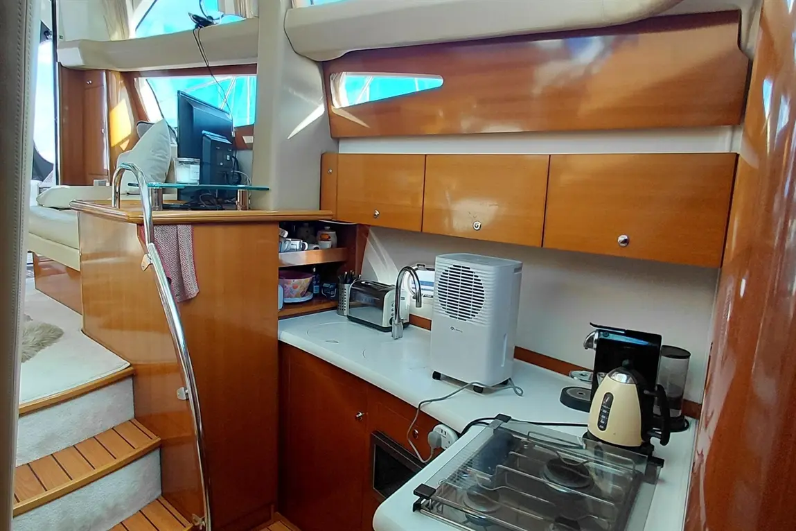 Modern boat kitchen featuring a stove, kettle, toaster, and cooler, with wooden cabinetry and staircase leading up.