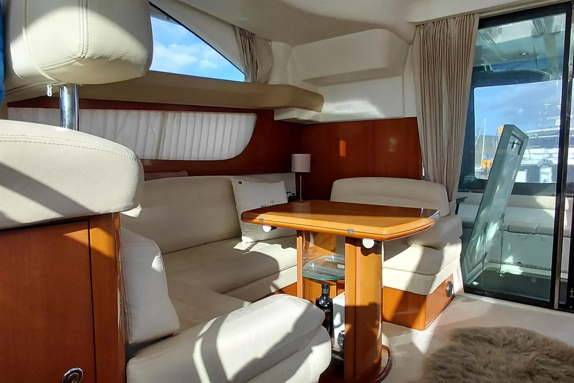 Luxury yacht interior featuring white leather seating, a wooden table, and large windows with scenic views.