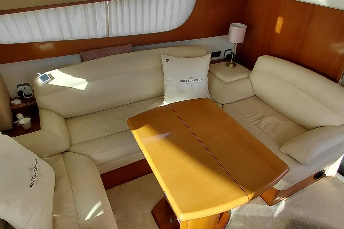 Interior of a yacht featuring beige leather sofas, a wooden table, a pink lamp, and a Moët & Chandon cushion.