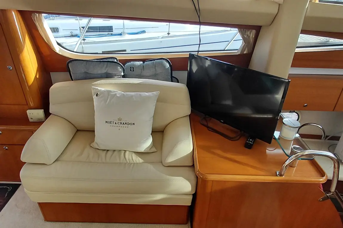 Interior of a luxury boat featuring a leather sofa with a Moët & Chandon cushion, a television, and a view of moored boats outside.