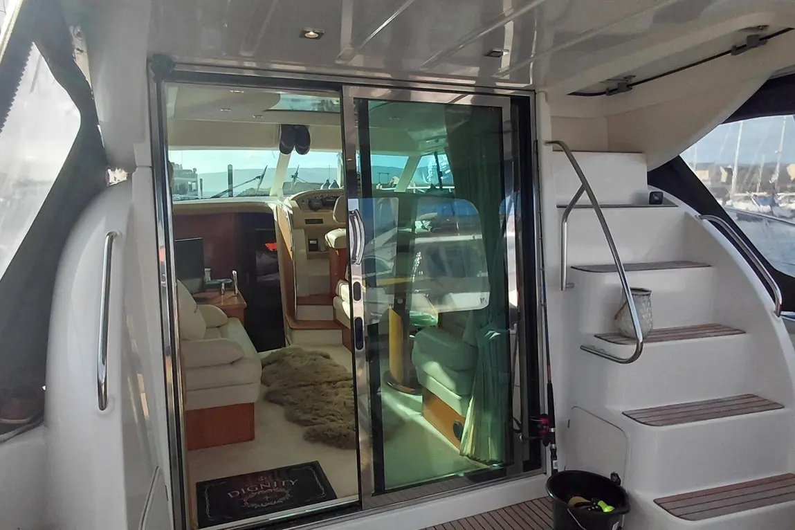 Interior of a yacht showing a lounge area through sliding glass doors, steps leading up and a welcome mat saying "DIGNITY.