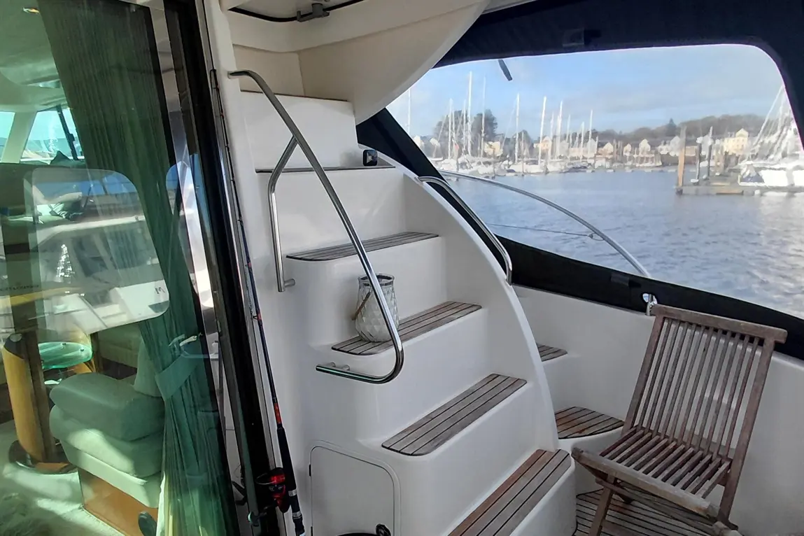 Interior of a yacht featuring a spiral staircase, a wooden chair, and a view of a marina with sailboats.