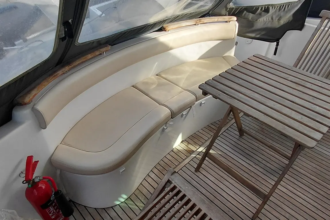 Interior of a boat featuring a cushioned bench, wooden table, and a fire extinguisher on the floor near the seating area.