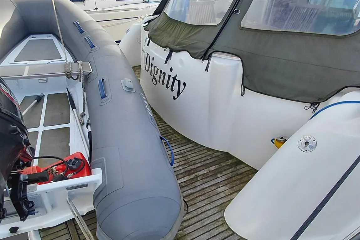 A grey inflatable boat next to a white vessel named "Dignity," with fuel and equipment visible on a wooden dock.