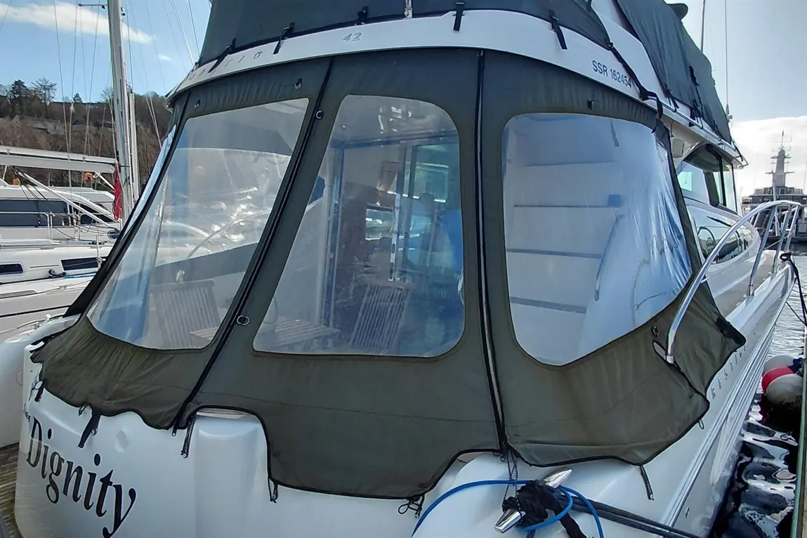 A docked boat named "Dignity" features clear vinyl curtains and a green cover, revealing interior seating and marina view.