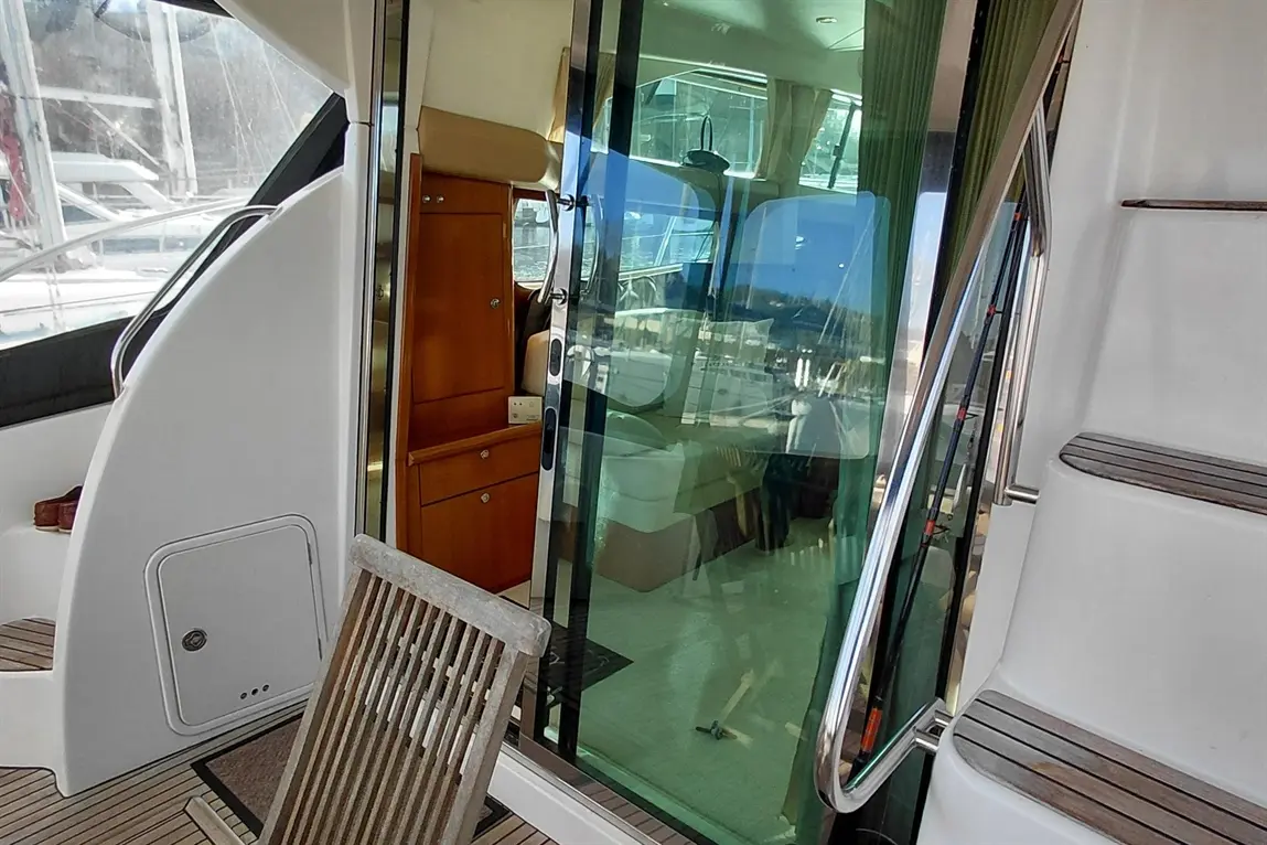 Deck view showing a glass door to a yacht cabin, wooden chair, and steps with a non-slip surface.