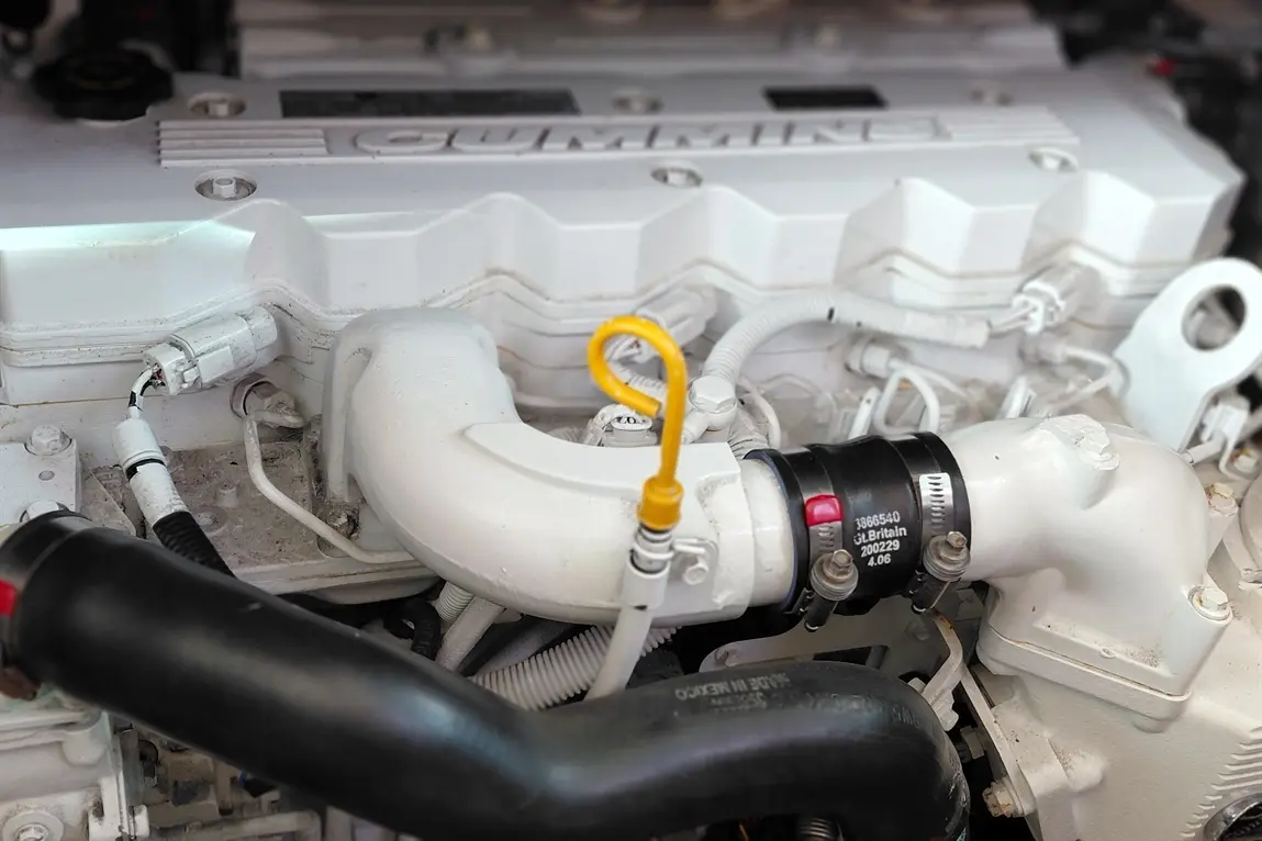 Close-up of a Cummins engine with visible hoses, connectors, and a yellow dipstick, highlighting automotive engineering details.
