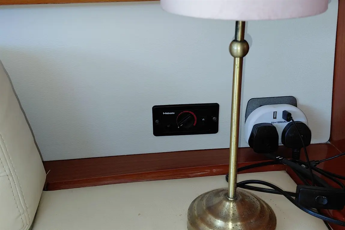 A brass lamp stands beside a black heater control panel and a white power socket with USB, on a cream-coloured surface.