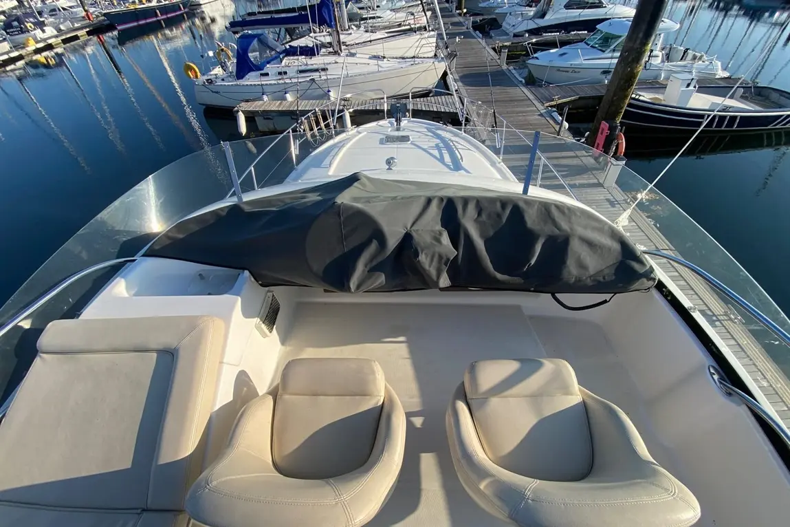 View from the bow of a boat with leather seats, a cover over the controls, and a marina filled with boats in the background.
