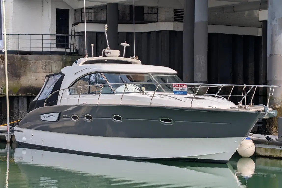 A sleek, grey and white motorboat labelled "FOR SALE" floats on calm water at a dock.