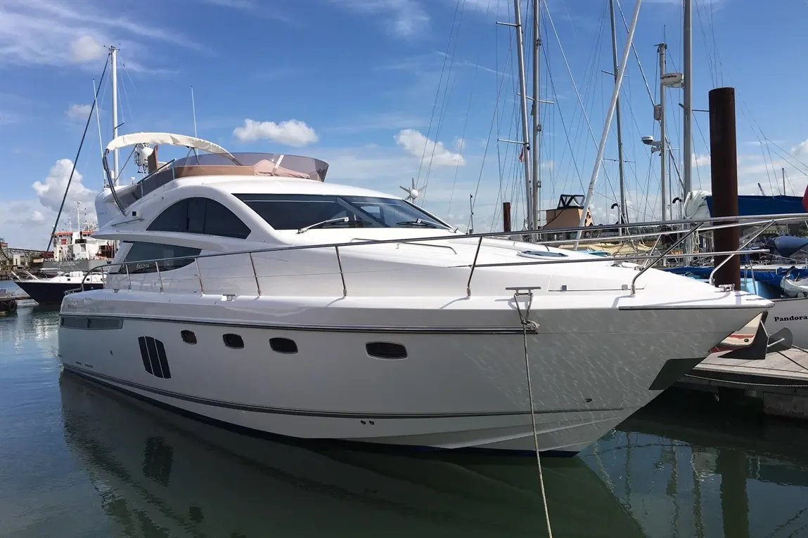 Luxury white yacht docked at a marina, surrounded by masts and boats under a blue sky with scattered clouds.