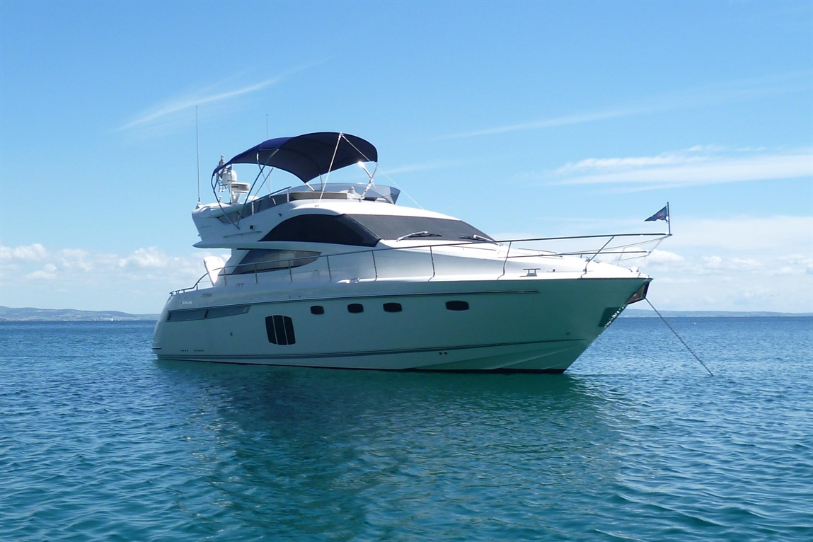 White luxury yacht anchored in clear blue water under a bright sky with light clouds in the background.