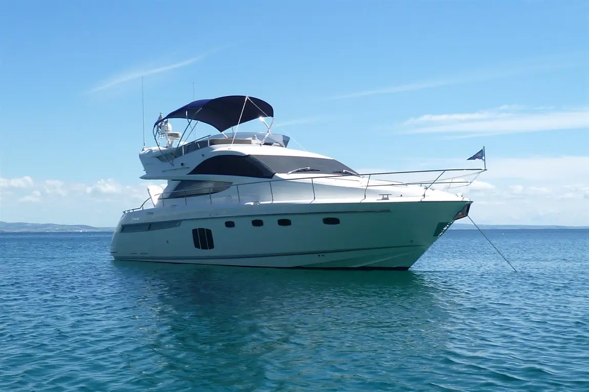 White luxury yacht anchored in clear blue water under a bright sky with light clouds in the background.