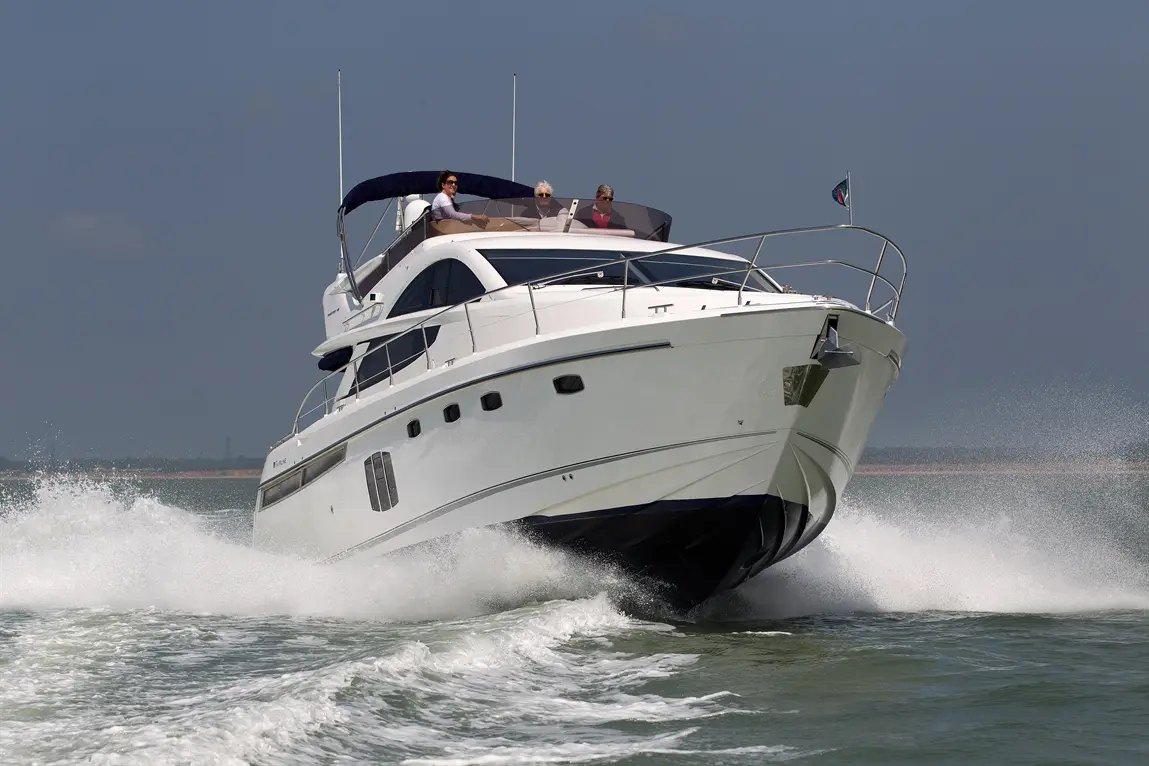 A luxurious motorboat speeds through water, creating a spray, with four people enjoying the ride on a sunny day.