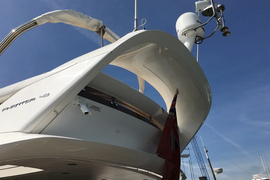 Phantom 43 yacht with a British flag, radar, and a clear blue sky in the background at a marina.