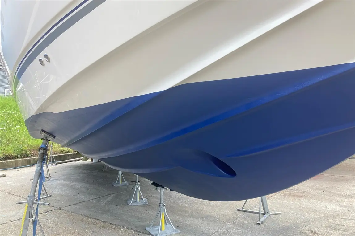 A boat resting on stands, featuring a sleek white and blue hull with visible waterline and hull design details.