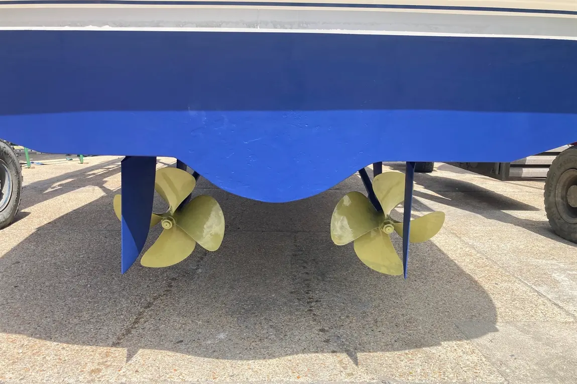 Underneath a blue boat, two yellow propellers are visible, set against a textured concrete surface.