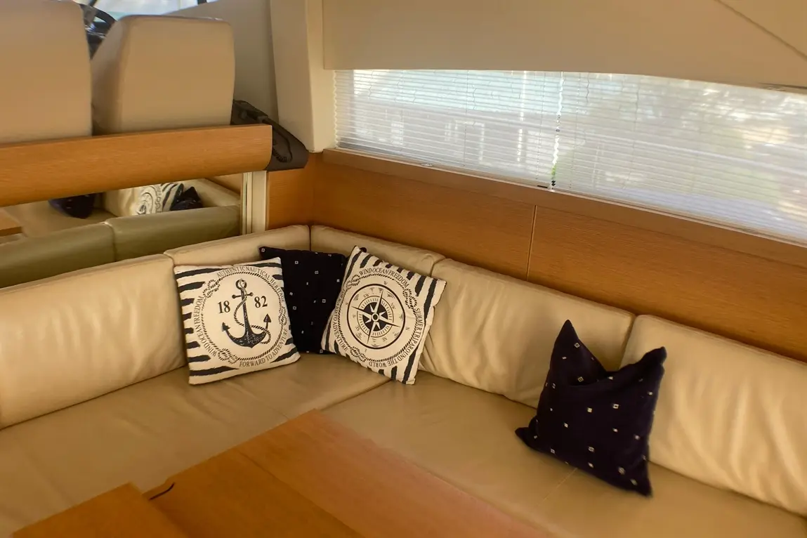 Interior of a yacht featuring a leather sofa, wooden table, and nautical-themed cushions with an anchor and compass design.